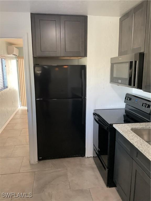 kitchen with light tile patterned floors, light stone counters, an AC wall unit, black appliances, and gray cabinets