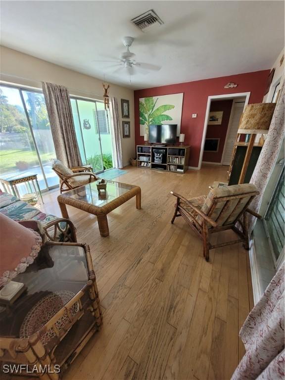 living room with ceiling fan, visible vents, and wood finished floors