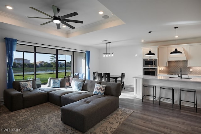 living room featuring a water view, ceiling fan, a raised ceiling, ornamental molding, and dark hardwood / wood-style floors