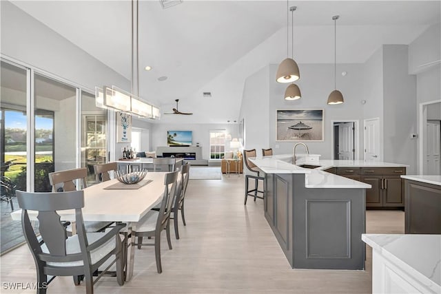 interior space featuring high vaulted ceiling, sink, hanging light fixtures, light hardwood / wood-style floors, and light stone countertops