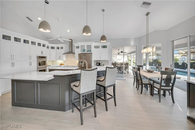 kitchen featuring a large island, decorative light fixtures, wall chimney exhaust hood, and appliances with stainless steel finishes