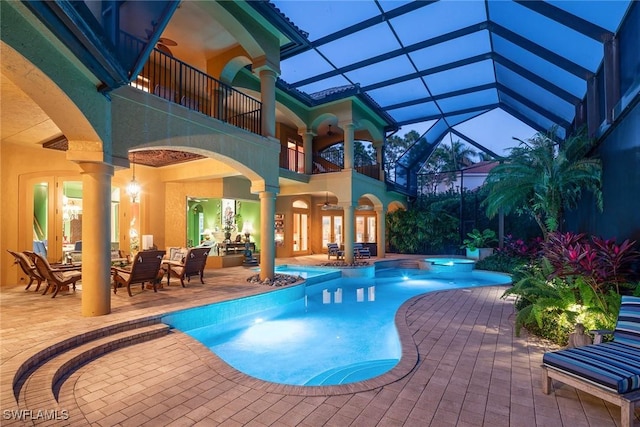 pool at dusk with ceiling fan, glass enclosure, a patio area, and an in ground hot tub