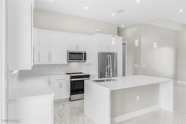 kitchen featuring sink, appliances with stainless steel finishes, white cabinetry, hanging light fixtures, and a center island with sink