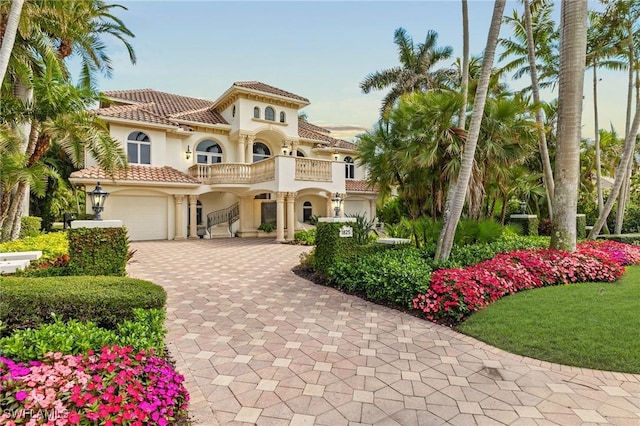 mediterranean / spanish house with a balcony, decorative driveway, an attached garage, stucco siding, and a tile roof