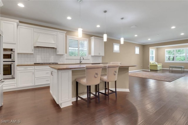 kitchen with a kitchen island, white cabinets, pendant lighting, and premium range hood