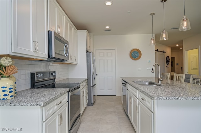 kitchen with a barn door, sink, appliances with stainless steel finishes, white cabinets, and pendant lighting