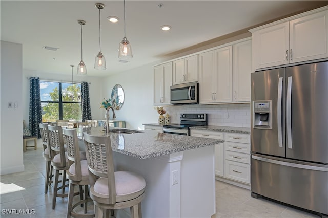 kitchen with an island with sink, light stone counters, appliances with stainless steel finishes, white cabinets, and pendant lighting