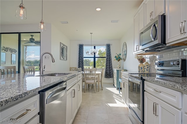 kitchen with appliances with stainless steel finishes, sink, backsplash, white cabinetry, and hanging light fixtures