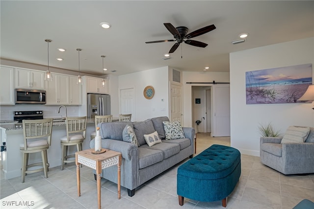 tiled living room with ceiling fan, a barn door, and sink