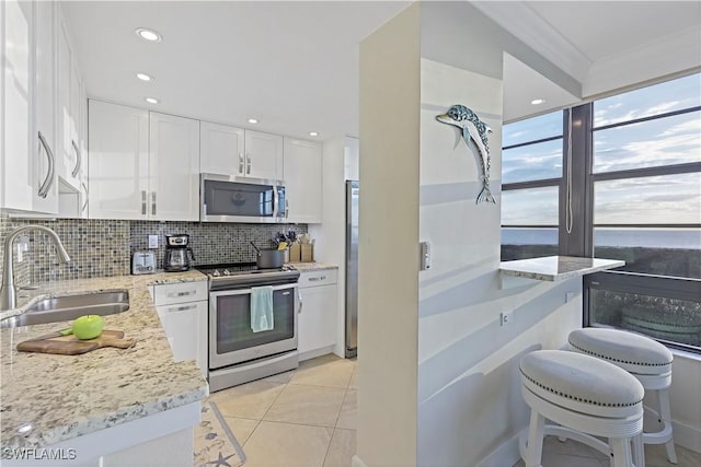 kitchen with sink, white cabinetry, stainless steel appliances, light stone countertops, and decorative backsplash