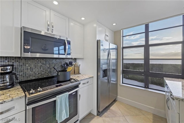 kitchen with white cabinetry, stainless steel appliances, light stone counters, and backsplash