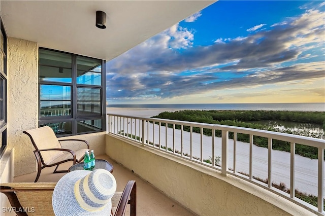 balcony at dusk featuring a water view