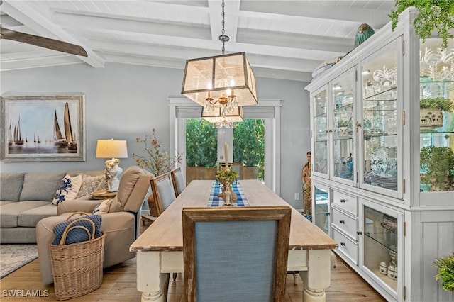 dining space with wood finished floors, lofted ceiling with beams, and a notable chandelier