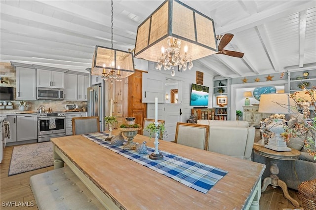 dining room with an inviting chandelier, light wood-style flooring, and vaulted ceiling with beams