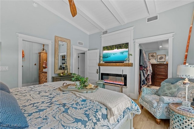 bedroom with a glass covered fireplace, lofted ceiling with beams, visible vents, and wood finished floors