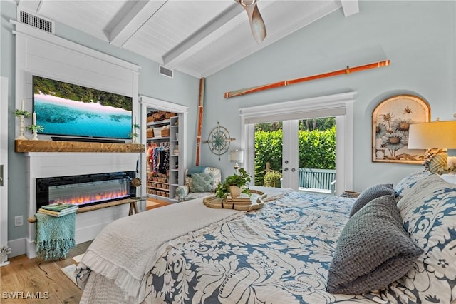 bedroom featuring a glass covered fireplace, visible vents, access to outside, wood finished floors, and lofted ceiling with beams