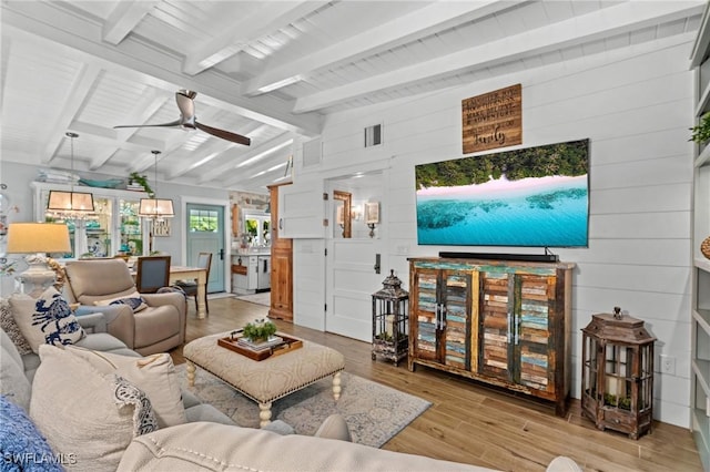 living area with visible vents, wood finished floors, wood walls, ceiling fan, and vaulted ceiling with beams