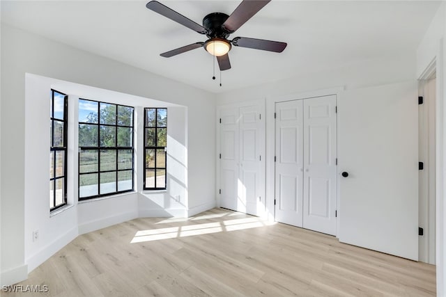 unfurnished bedroom with multiple closets, ceiling fan, and light wood-type flooring