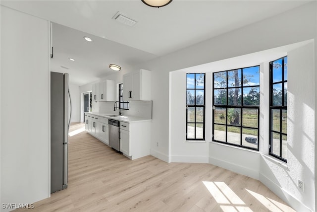 kitchen with appliances with stainless steel finishes, sink, white cabinets, and light hardwood / wood-style floors