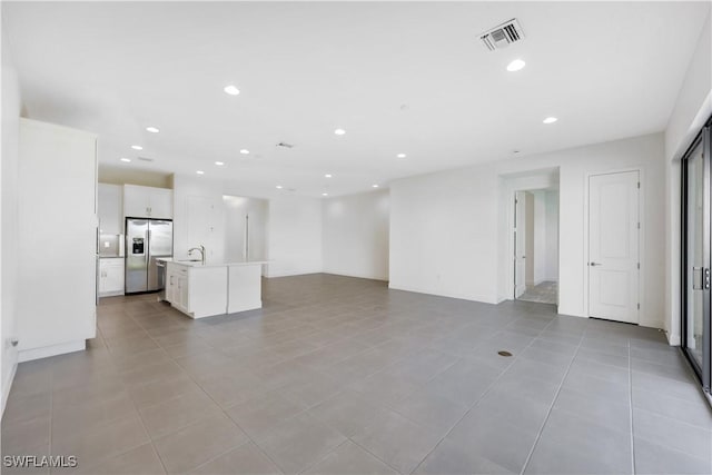 unfurnished living room featuring light tile patterned floors, visible vents, recessed lighting, and a sink