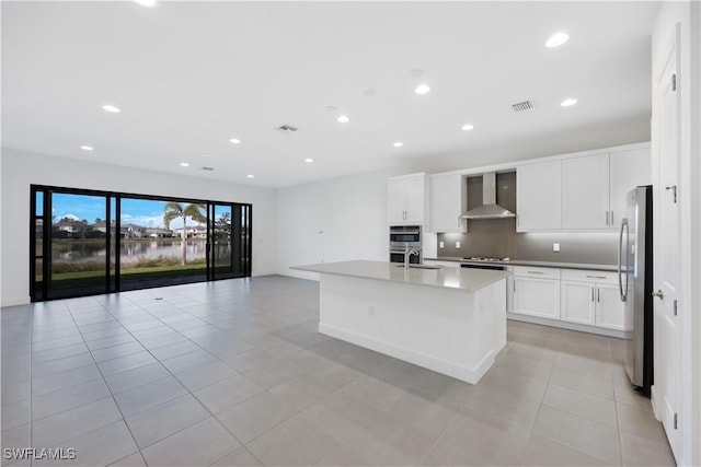 kitchen featuring visible vents, wall chimney range hood, open floor plan, stainless steel appliances, and white cabinetry