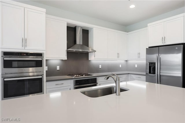 kitchen featuring a sink, appliances with stainless steel finishes, wall chimney exhaust hood, and white cabinets