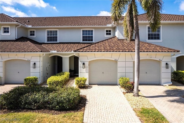 view of front of property with a tiled roof, decorative driveway, an attached garage, and stucco siding