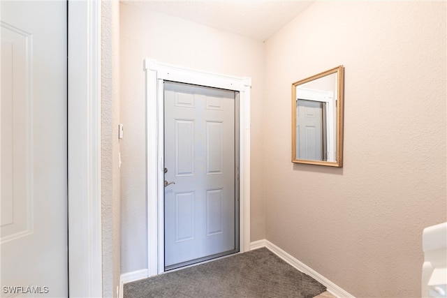 entryway with carpet floors, a textured wall, and baseboards