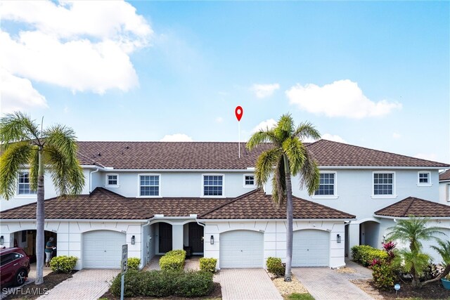 view of front of property with decorative driveway, an attached garage, a tile roof, and stucco siding