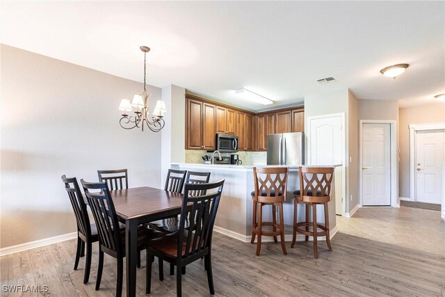 dining area with baseboards, an inviting chandelier, visible vents, and light wood-style floors