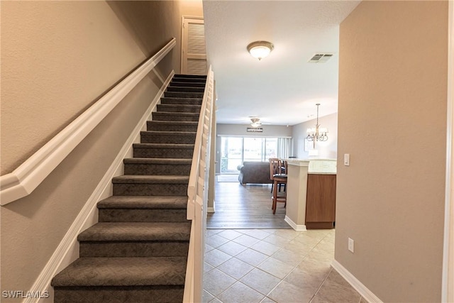 stairway with a chandelier, tile patterned flooring, visible vents, and baseboards