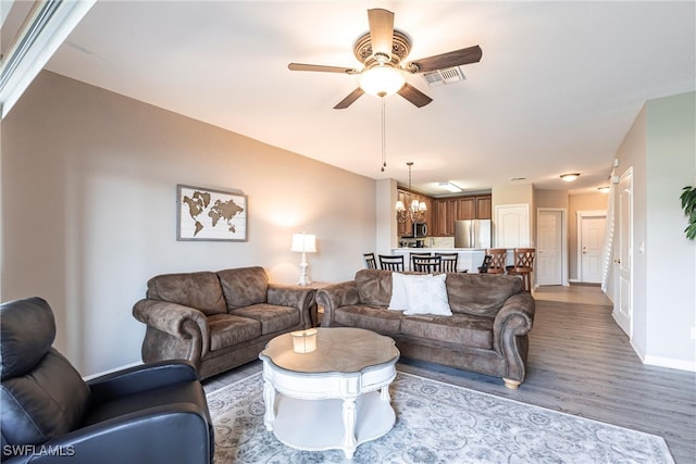 living room featuring ceiling fan with notable chandelier, visible vents, baseboards, and wood finished floors