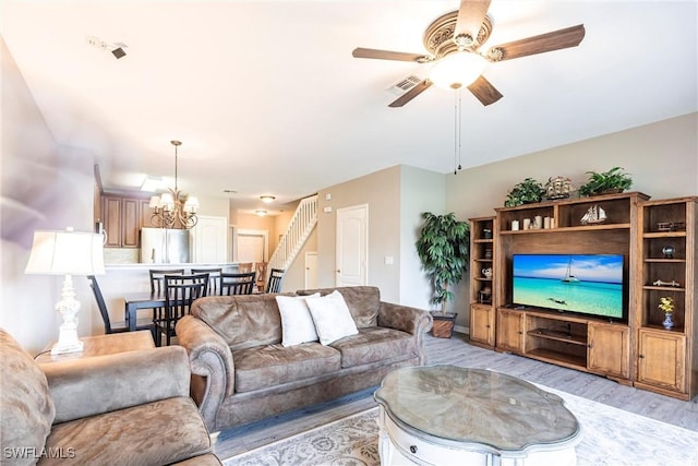 living area featuring ceiling fan with notable chandelier, light wood-type flooring, and stairs