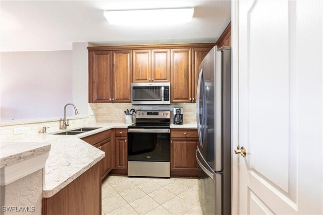 kitchen with stainless steel appliances, brown cabinetry, a peninsula, and a sink