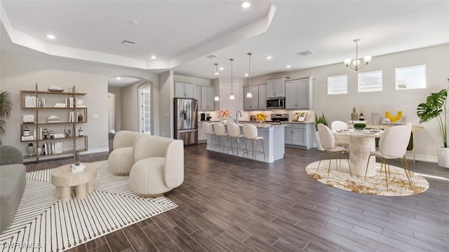 living room with wood tiled floor, a raised ceiling, arched walkways, and recessed lighting