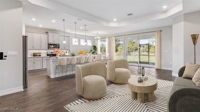 living room with an inviting chandelier, a tray ceiling, and dark wood-type flooring