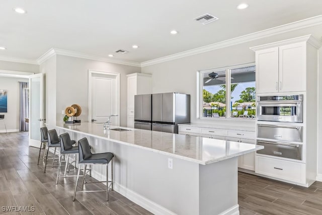 kitchen with a kitchen island with sink, a breakfast bar area, white cabinets, and appliances with stainless steel finishes