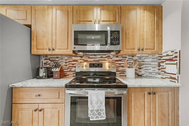 kitchen with light brown cabinetry, appliances with stainless steel finishes, light stone counters, and decorative backsplash