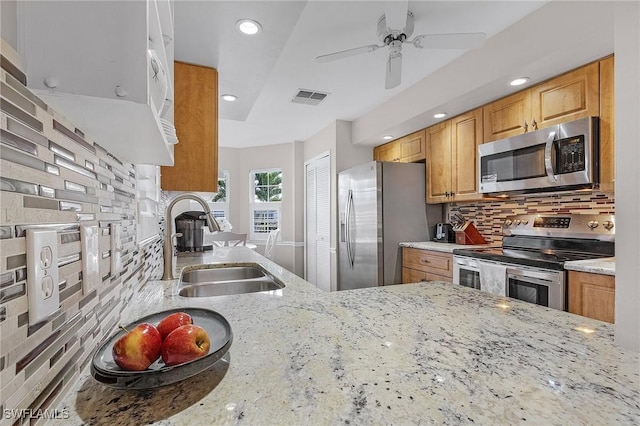 kitchen featuring appliances with stainless steel finishes, sink, backsplash, ceiling fan, and light stone countertops