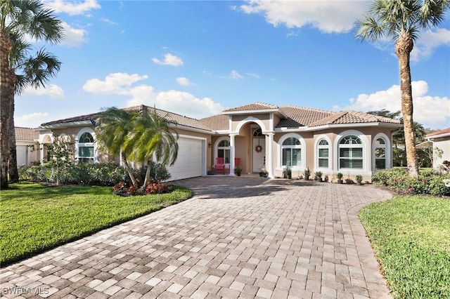 mediterranean / spanish-style home featuring decorative driveway, a tile roof, stucco siding, a front yard, and a garage