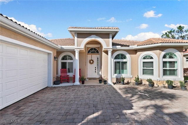 view of exterior entry featuring an attached garage, a tile roof, and stucco siding