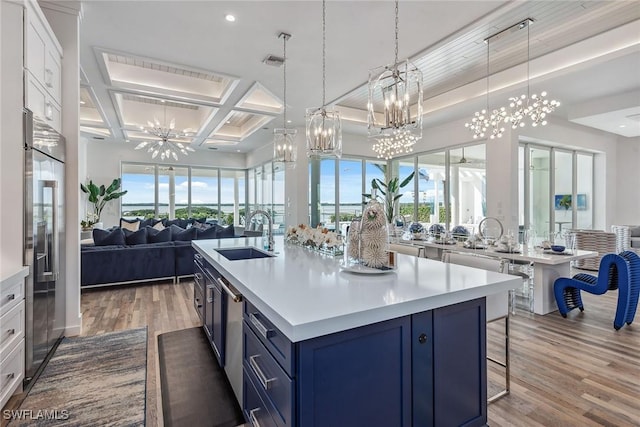 kitchen featuring light wood finished floors, open floor plan, blue cabinets, a kitchen island with sink, and a sink