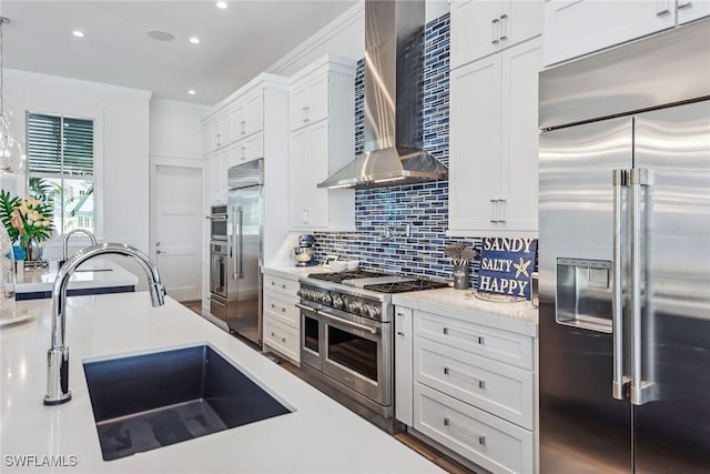 kitchen with high end appliances, a sink, light countertops, wall chimney range hood, and backsplash