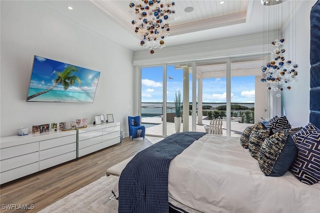 bedroom featuring access to outside, a tray ceiling, wood finished floors, and ornamental molding