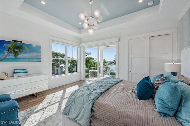 bedroom with access to outside, a raised ceiling, and wood finished floors