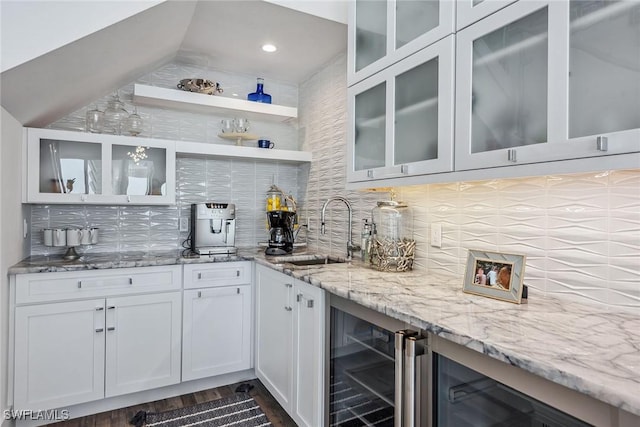 kitchen featuring light stone counters, white cabinetry, a sink, and backsplash