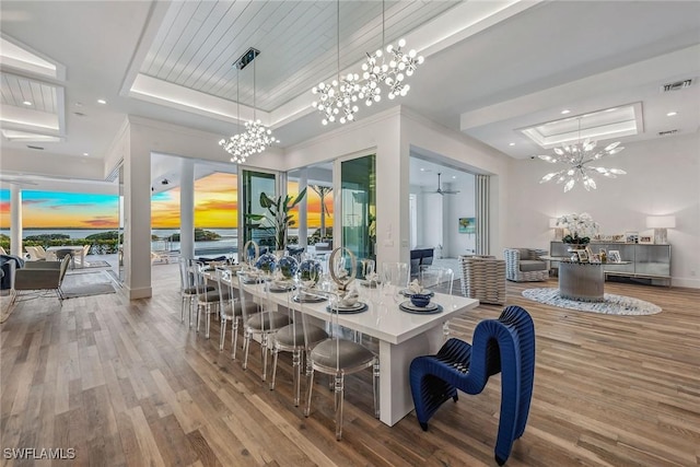 dining space with a raised ceiling, visible vents, crown molding, and wood finished floors