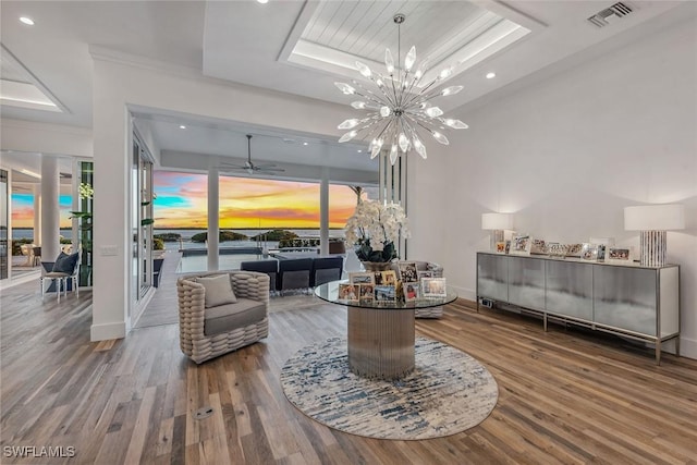 living area with wood finished floors, visible vents, baseboards, a raised ceiling, and an inviting chandelier