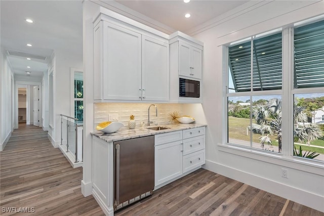 bar with high quality fridge, wood finished floors, a sink, black microwave, and backsplash