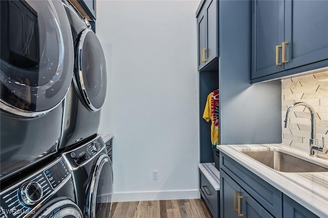 washroom featuring stacked washer and clothes dryer, cabinet space, a sink, wood finished floors, and baseboards